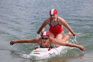 Zwei Schwimmerinnen auf einem Surfbrett im Wasser.