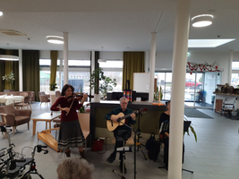 Eine Violin- und Gitarrenaufführung in einem Gemeinschaftsraum mit Pflanzen.