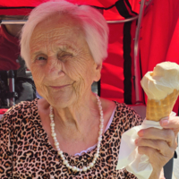 Ältere Frau mit weißem Haar hält ein Eis in der Waffel und lächelt.