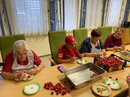 Ältere Menschen und ein Junge schneiden frisches Obst in einer hellen Küche.