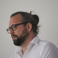 Ein Mann mit zugebundenen Haaren und Brille sieht zur Seite.
