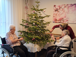 Drei Frauen in Rollstühlen dekorieren gemeinsam einen Weihnachtsbaum.