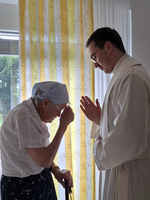 Ein Priester segnet eine ältere Dame in einem hellen Raum.