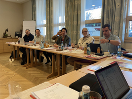 Sechs Personen sitzen an einem Tisch in einer Besprechung.