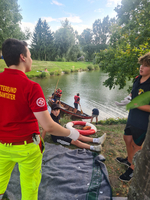 Ein Sanitäter erklärt Jugendkinder der Feuerwehr Erste Hilfe. Im Hintergrund sind zwei Jugendkinder in einer Zille.