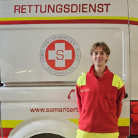 Ein Rettungsdienstmitarbeiter steht vor einem Krankenwagen.