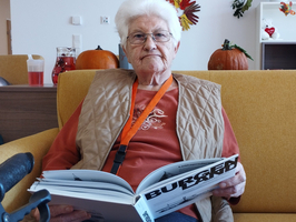 Eine ältere Frau sitzt auf einer Couch und liest ein Buch.