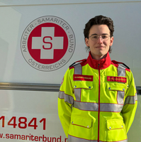 Ein Sanitäter in Uniform steht vor einem Rettungsauto des Samariterbundes.