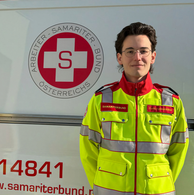 Ein Sanitäter in Uniform steht vor einem Rettungsauto des Samariterbundes.