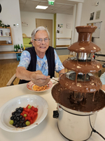 Eine ältere Frau genießt frisches Obst mit einer Schokoladenfontäne.