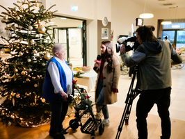 Eine ältere Frau spricht mit einer Reporterin vor einem Weihnachtsbaum.