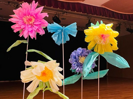 Bunte Papierblumen in verschiedenen Formen und Farben stehen auf einer Bühne.