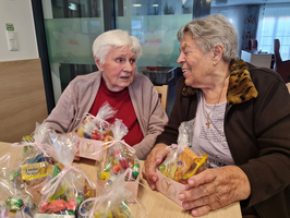 Zwei ältere Frauen unterhalten sich fröhlich über Geschenktüten mit Süßigkeiten.