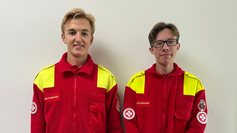 Zwei junge Menschen in roten Uniformen des Rettungsdienstes stehen nebeneinander.