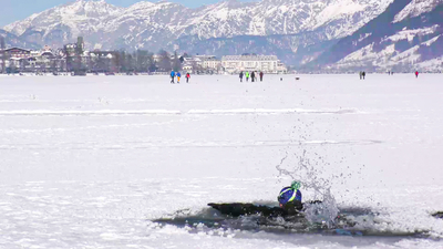 Ein Sprung ins Eiswasser mit schneebedeckten Bergen im Hintergrund.