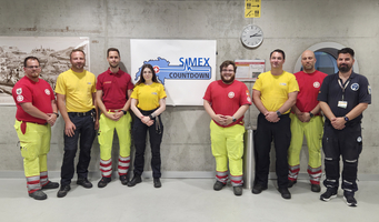 Gruppenbild von Rettungskräften mit unterschiedlichfarbigen Uniformen vor einem Countdown-Schild.