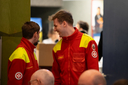 Zwei Männer in roten Rettungsdienstuniformen unterhalten sich lächelnd.