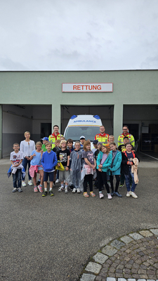 Gruppe von Kindern und Rettungskräften vor einem Rettungswagen.