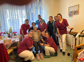 Gruppe von Pflegekräften mit älterer Frau in einem Wohnraum.