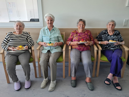 Vier ältere Frauen sitzen nebeneinander und halten Teller mit Kuchen.