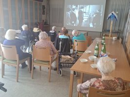 Ältere Menschen schauen gemeinsam einen Film in einem Veranstaltungsraum.