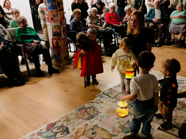 Kinder führen eine Aufführung für ältere Menschen durch, mit Laternen und Kostümen.