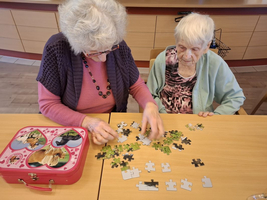 Zwei ältere Frauen puzzeln gemeinsam an einem Tisch.