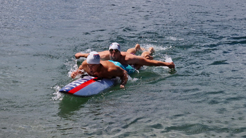 Zwei Männer schwimmen auf einem Rettungsbrett in flachem Wasser.