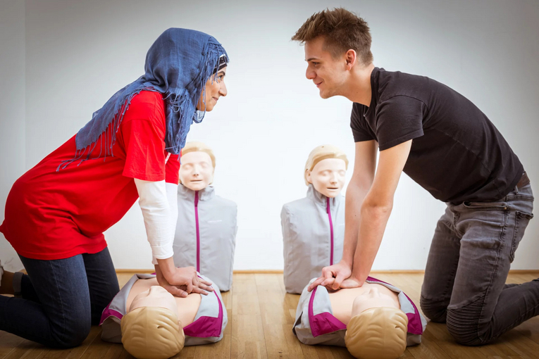 Zwei Personen gegenüber, die Herzdruckmassage auf Puppen üben