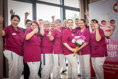 Ein fröhliches Team in pinken Uniformen posiert mit Daumen hoch und Blumen.