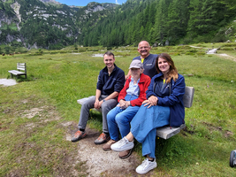 Vier Personen sitzen auf einer Bank in einer grünen, bergigen Landschaft.