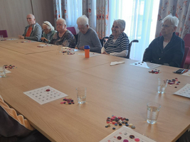 Senioren spielen Bingo an einem Tisch in einem Gemeinschaftsraum.