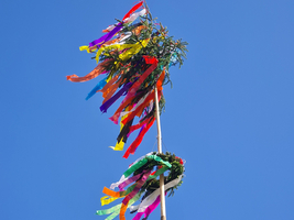 Bunt geschmückter Maibaum mit bunten Bändern vor klarem blauen Himmel.