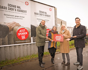 Oliver Löhlein und Susanne Drapalik mit zwei weiteren Personen vor Plakatwand mit Sujet Schau ma, dass sichs ausgeht, halten rotes Schild mit Slogan in der Hand, winterliche Atmosphäre