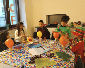 Kinder im LernLEO in verschiedenen Kostümen, bemalen Luftballons, Tisch mit Bastelablage