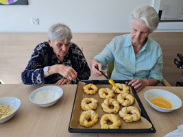 Zwei ältere Frauen bereiten frisch gebackene Brötchen auf einem Tisch vor.