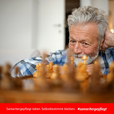 Mann der vor einem Schachbrett sitzt, Nahaufnahme, sein Kopf nicht ganz sichtbar, im Vordergrund verschwommene hölzerne Schachfiguren