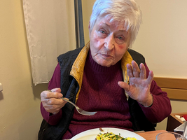 Eine ältere Frau sitzt am Tisch und genießt ihr Frühstück.