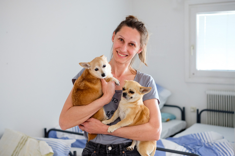 Junge Frau mit ihren zwei Hunden am Arm steht in ihrem Zimmer