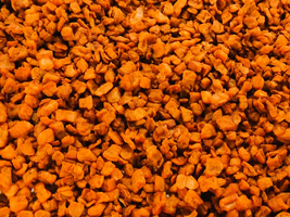 Zerkleinerte orangefarbene Stücke in einem breiten, gleichmäßigen Muster angeordnet.