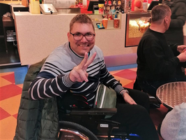 Ein Mann im Rollstuhl lächelt und zeigt ein Peace-Zeichen.