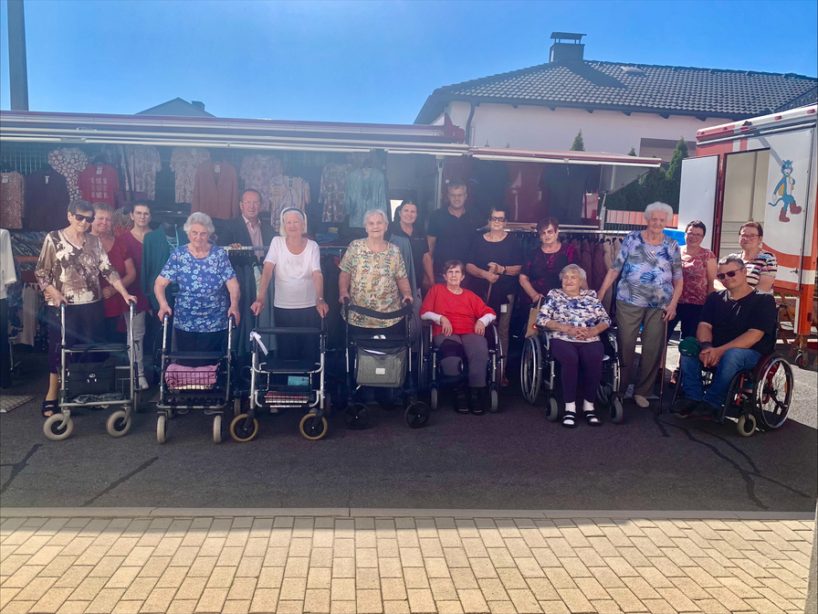 Gruppierung von Menschen mit Rollstühlen vor einem Verkaufsstand im Freien.