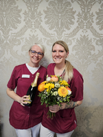 Zwei Frauen in Uniform halten Sekt und einen bunten Blumenstrauß.