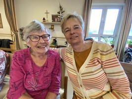 Zwei Frauen lächeln freundlich nebeneinander in einem gemütlichen Raum.