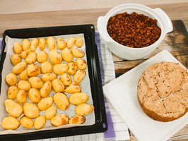 Ein Tablett mit kleinen gebackenen Snacks, eine Schüssel mit Fleisch und ein Brot.