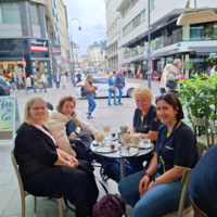 Vier Frauen sitzen an einem Tisch mit Getränken in einem Straßencafé.