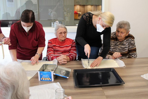 Ältere Frauen und Betreuerin backen gemeinsam an einem Tisch.