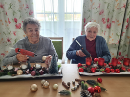 Zwei ältere Frauen basteln weihnachtliche Dekorationen am Tisch.