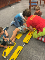 Kinder üben Erste Hilfe mit einer Tragbahre und unterstützen einen verletzten Kameraden.