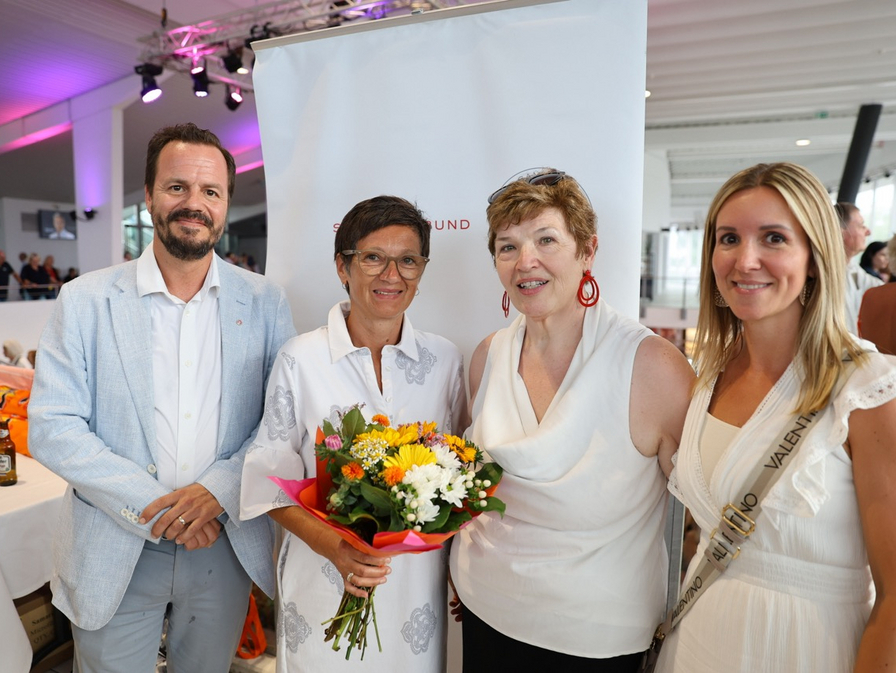 Vier Personen posieren gemeinsam, eine hält Blumen in der Hand.